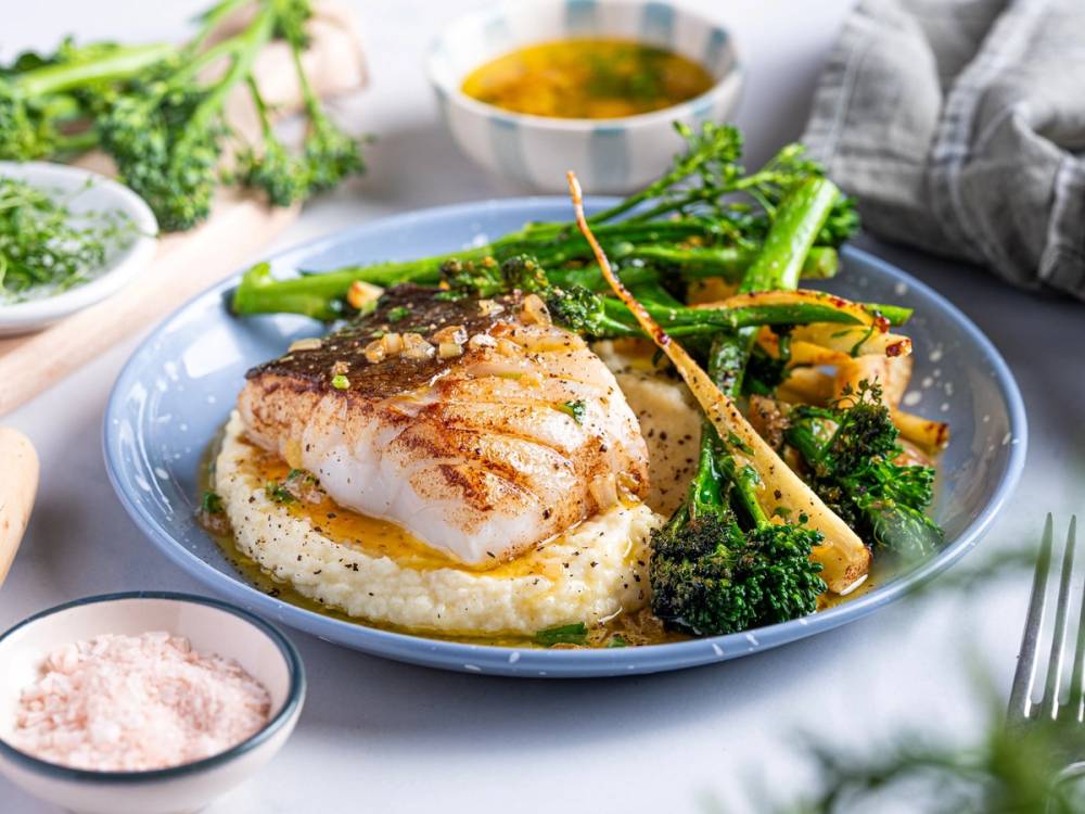 Skrei med soya smør servert med grønnsaker som brokkoli og asparges på en tallerken.