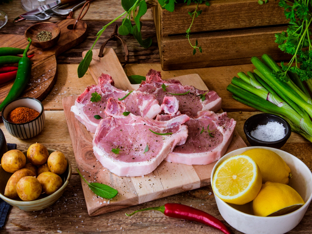 Stekte koteletter med sitron, grønnsaker og krydder på et trefat, klar til å bli stekt eller servert.