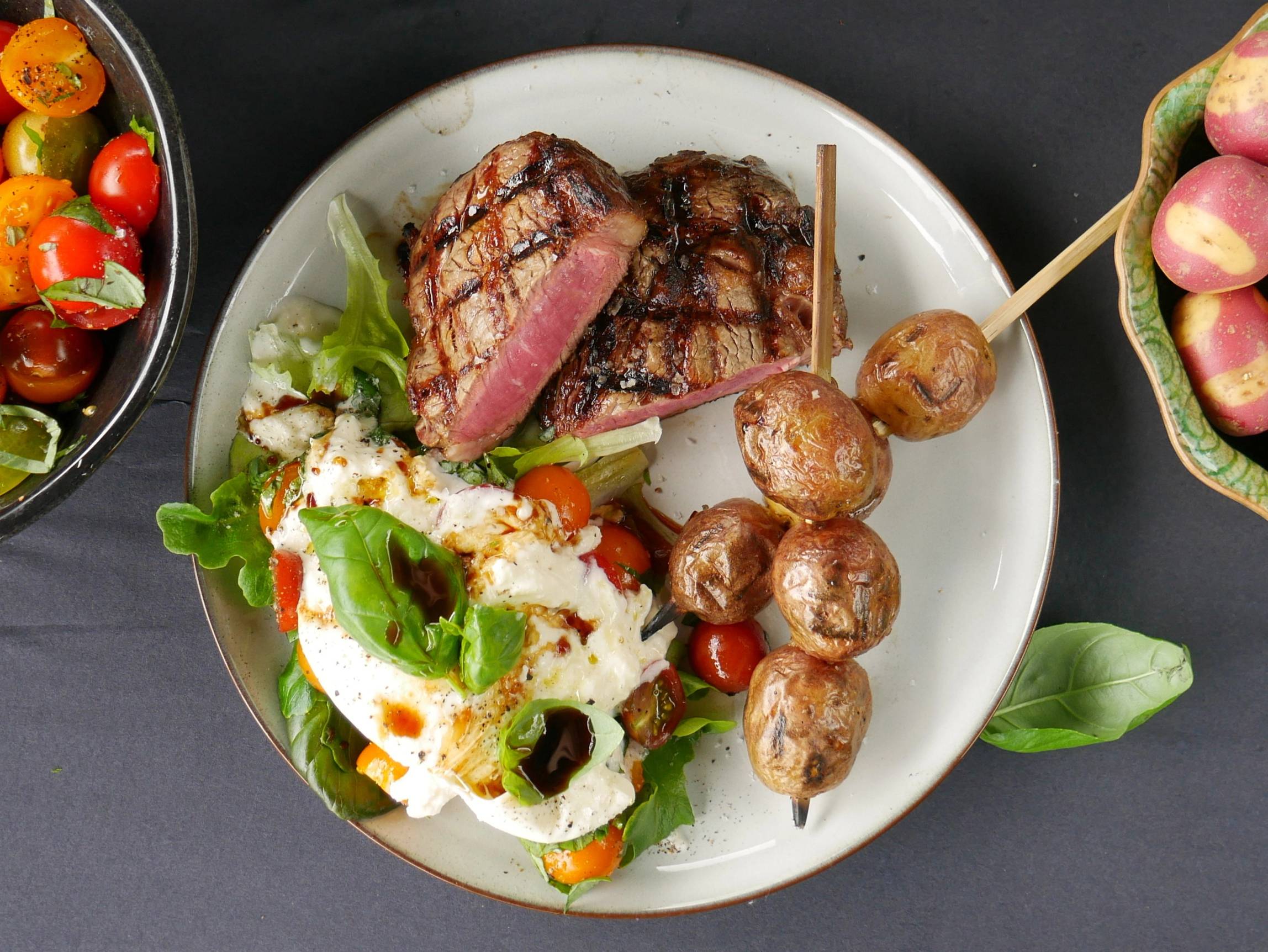 Stekt biff med salat og grillet sopp på en hvit tallerken, omgitt av andre retter og grønnsaker.