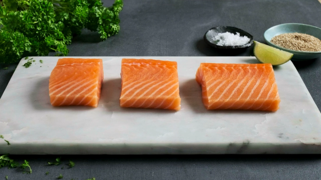 Tre laksefileter ligger på en skjærebrett, klare til å bli stekt.