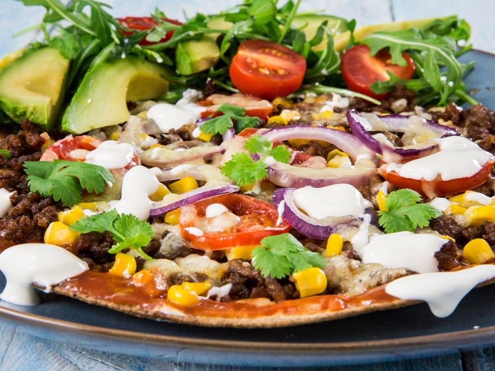 Tortillapizza med kjøttdeig, tomater, mais, rømme, løk, avokado og frisk koriander på toppen.