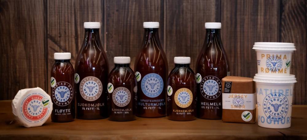 En rekke med brune glassflasker med hvite korker, plassert foran en eske og en liten kremboks, på en treoverflate.