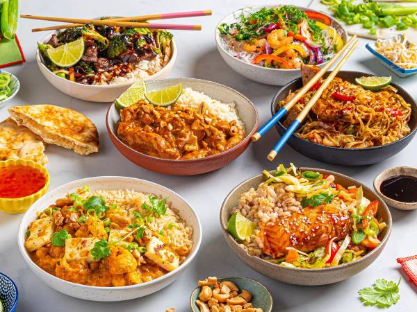 Et utvalg av asiatiske retter på bordet, inkludert ris, nudler og grønnsaker, med spisepinner og små skåler med saus.