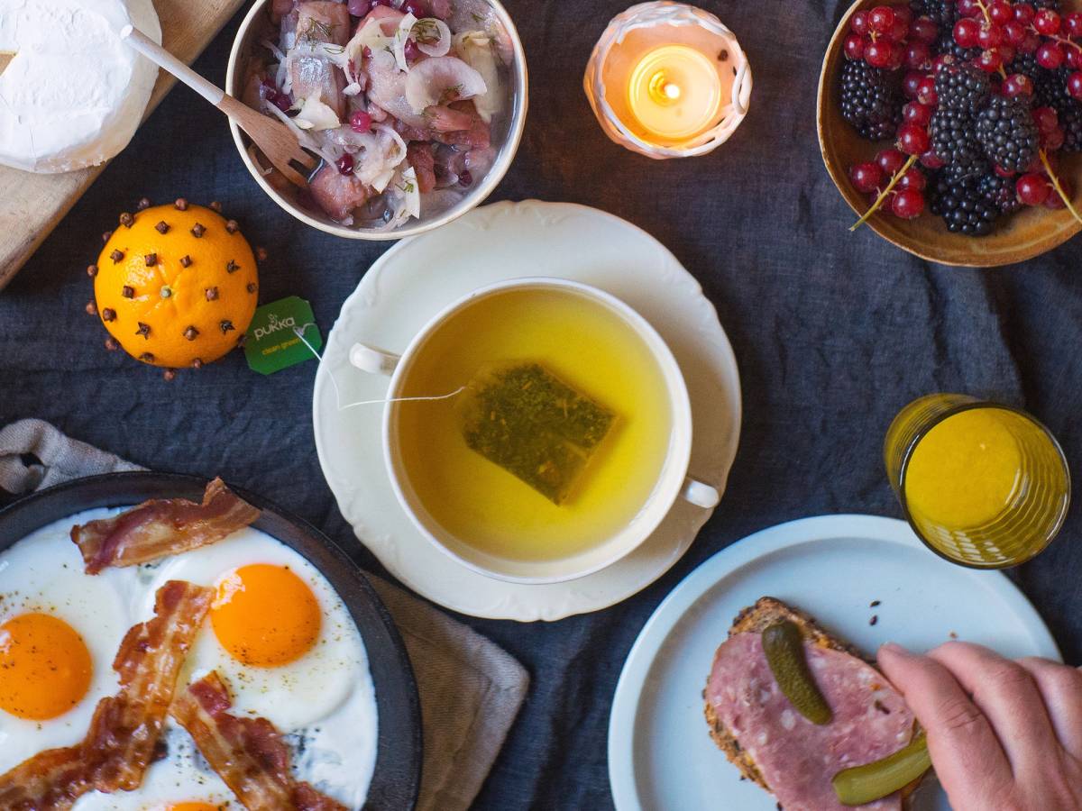 En julefrokost med egg, pølser, bær, ost og en kopp med grønn te på et bord.