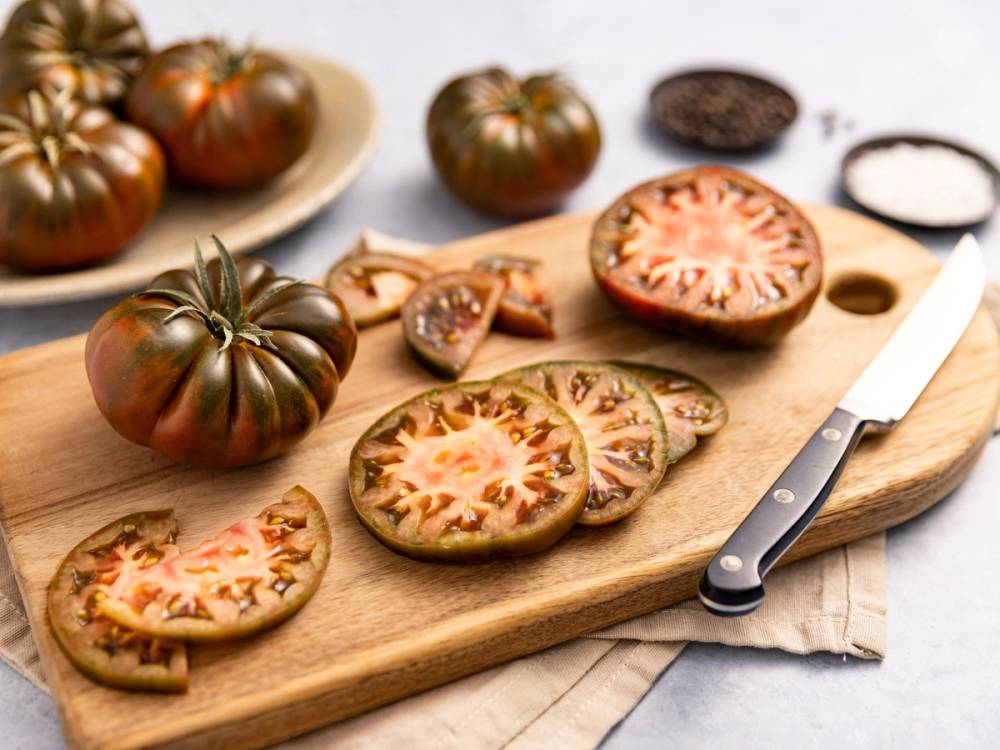 Skarpe tomater og tomatskiver på en skjærebrett med en kniv og en liten skål med salt ved siden av.