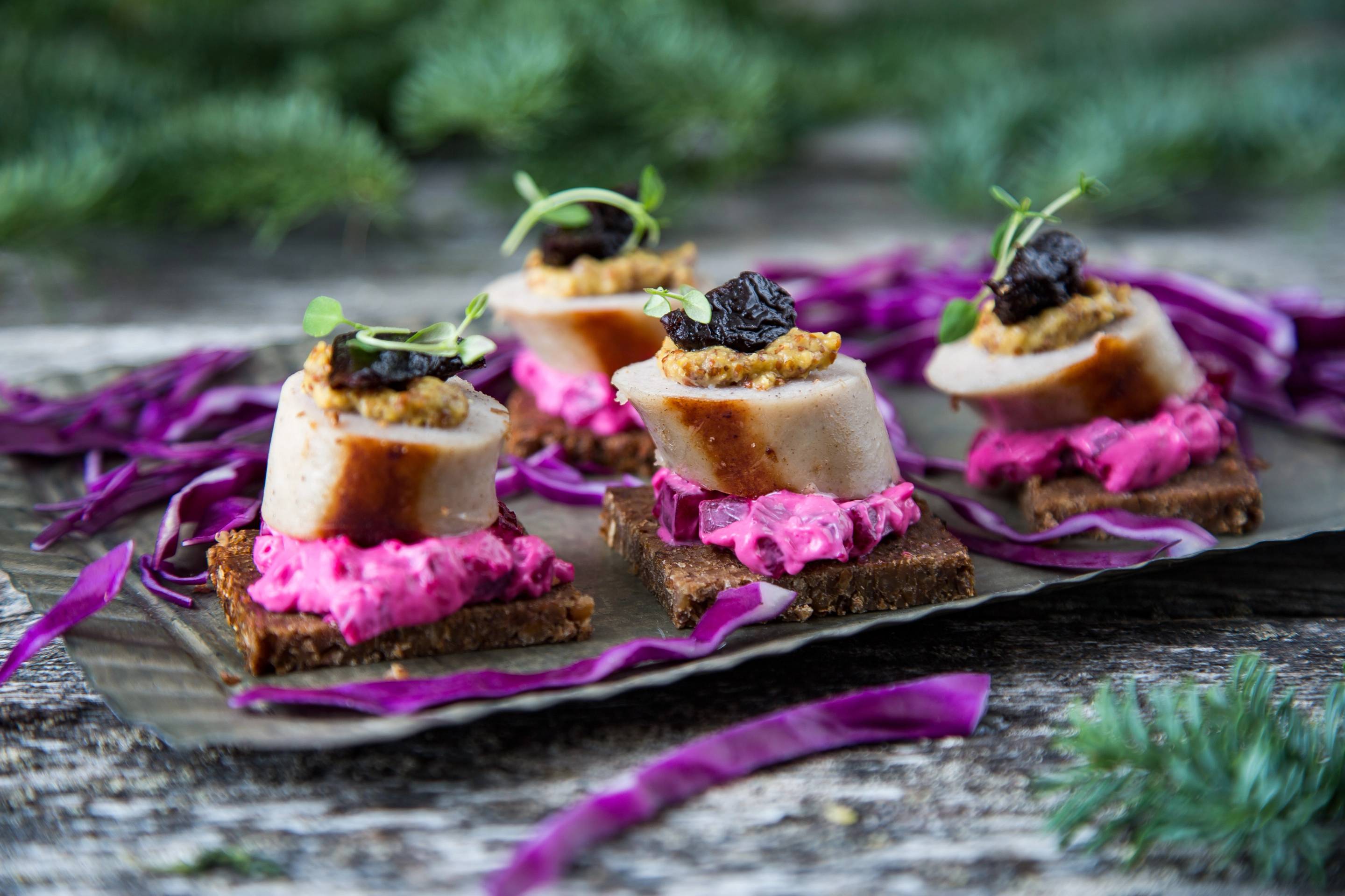 Pølsepinxos med pølse og svart trøffel på små brødskiver, pyntet med urter, ser ut til å være på et serveringsfat.