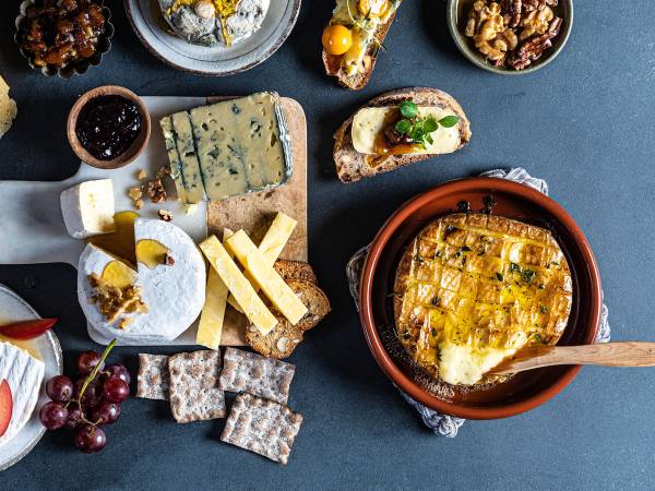 Et ostefat med ulike typer ost, kjeks, druer og tilbehør på et mørkt bord.