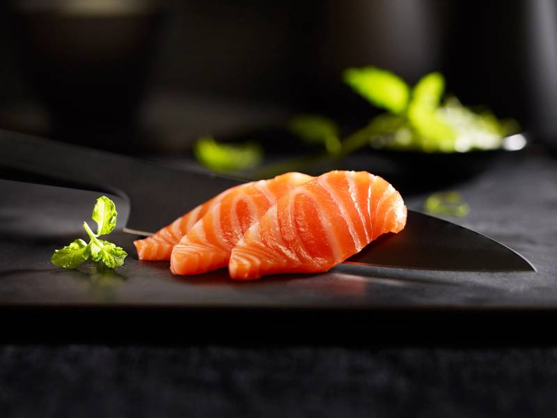 To skiver laksefilet med en liten kvist sitron og noen grønne urter på en svart tallerken.