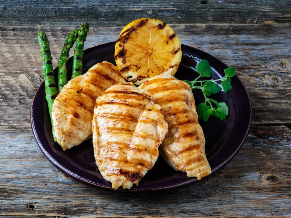 Grillet kyllingfilet med asparges og en liten porsjonskake på en svart tallerken, plassert på et rustikt trebord.