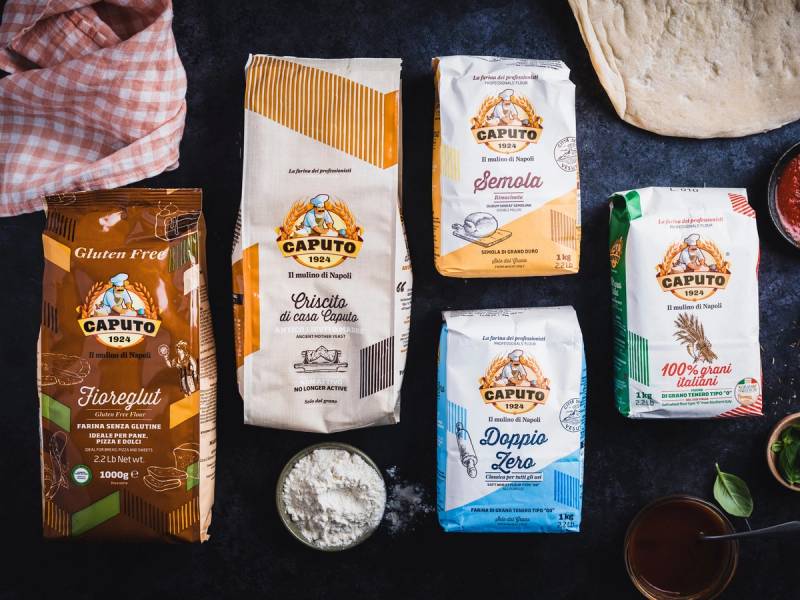 Ulike typer av mel, inkludert hvetemel og fullkornsmel, på et svart bord med noen grønne blader og en liten bolle med mel.