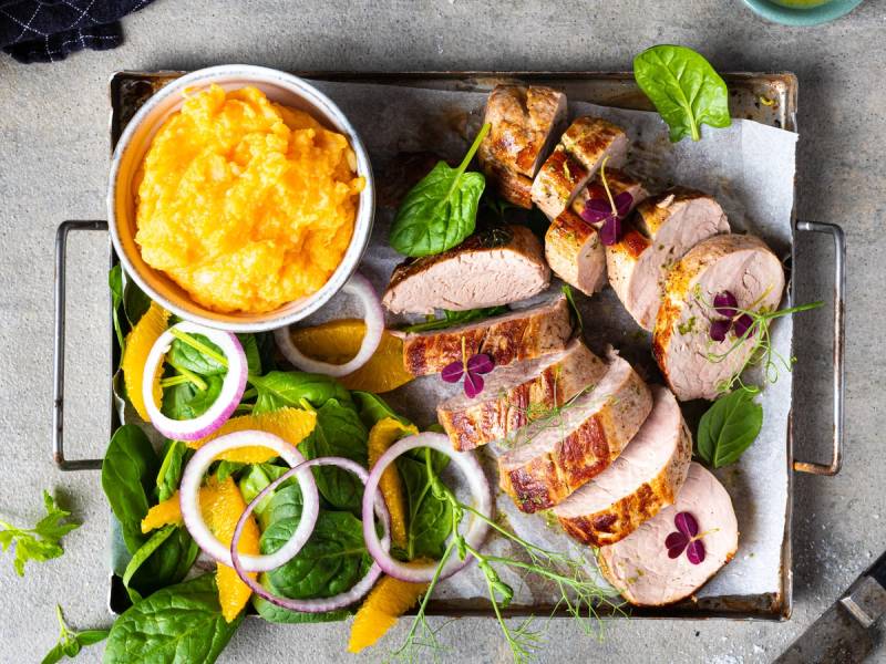 Svinefilet skåret i skiver med en side av potetmos og grønnsaker på et serveringsfat.