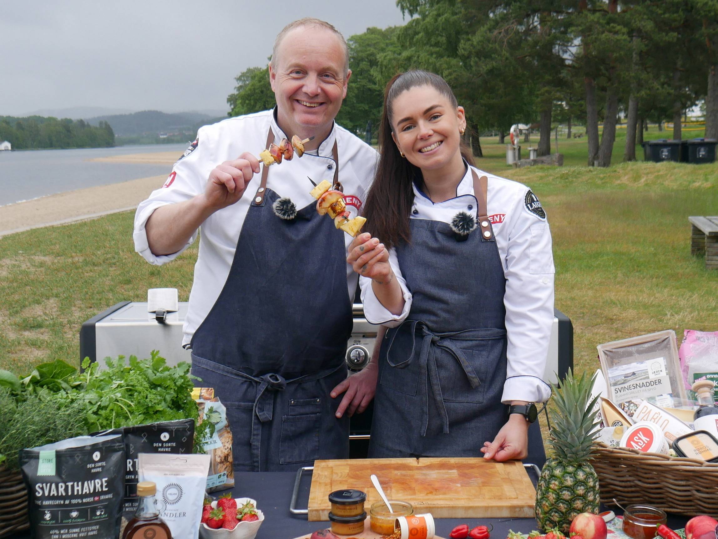 To personer med forkle som lager mat på en utendørs grillfest ved sjøen i Kristiansand, juni 2025.
