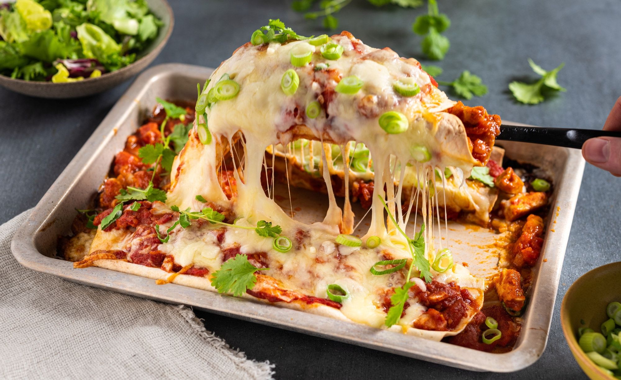 En ildfast form med enchiladas fylt med kylling og dekket med smeltet ost, garnert med frisk koriander og grønn løk.