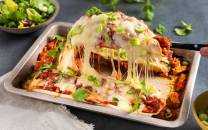 En ildfast form med enchiladas fylt med kylling og dekket med smeltet ost, garnert med frisk koriander og grønn løk.