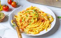 Pasta med fetaost og cherrytomater på en hvit tallerken, omgitt av tomater og krydderurter, klar til servering.