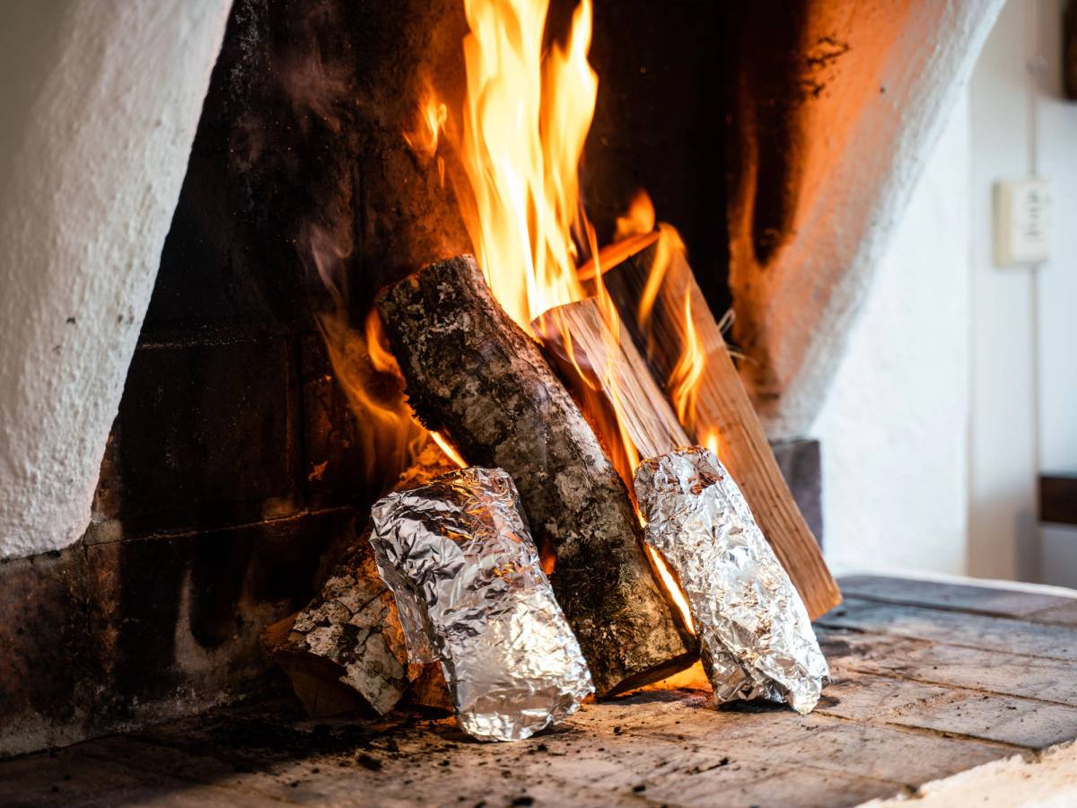Vedovn med brennende ved som avgir varme og lys, omgitt av steiner og murvegg.