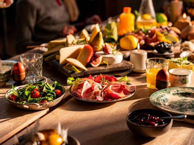 Et bord dekket med ulike retter, frukt, grønnsaker, og drikkevarer til en måltidssituasjon.