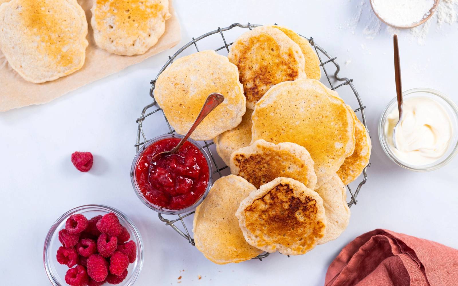 Ferske sveler på en rist med bær og syltetøy, omgitt av en skje med rømme og friske bringebær.