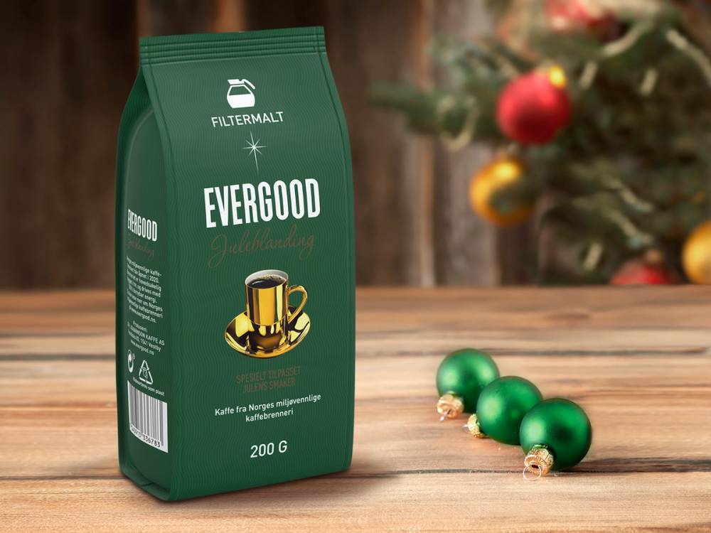 En pose med Evergood julekaffe 2022 ved siden av tre grønne julekuler, med julepyntet tre i bakgrunnen.