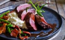 Rensdyrfilet med saus, servert med potetmos og grønnsaker på en svart tallerken.