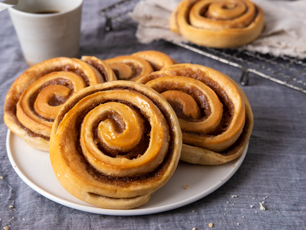 Kanelboller på en tallerken med en kopp kaffe i bakgrunnen.