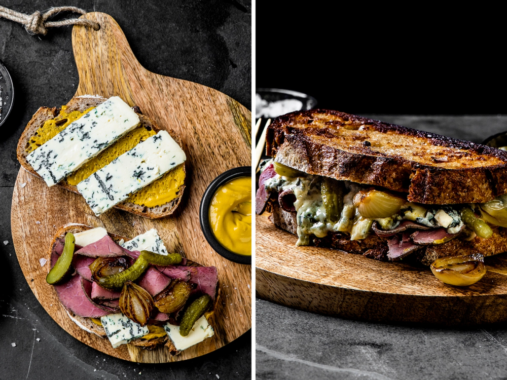 Et ostesmørbrød med blåmuggost og skinke på en treplate, med en liten skål med sennep ved siden av.