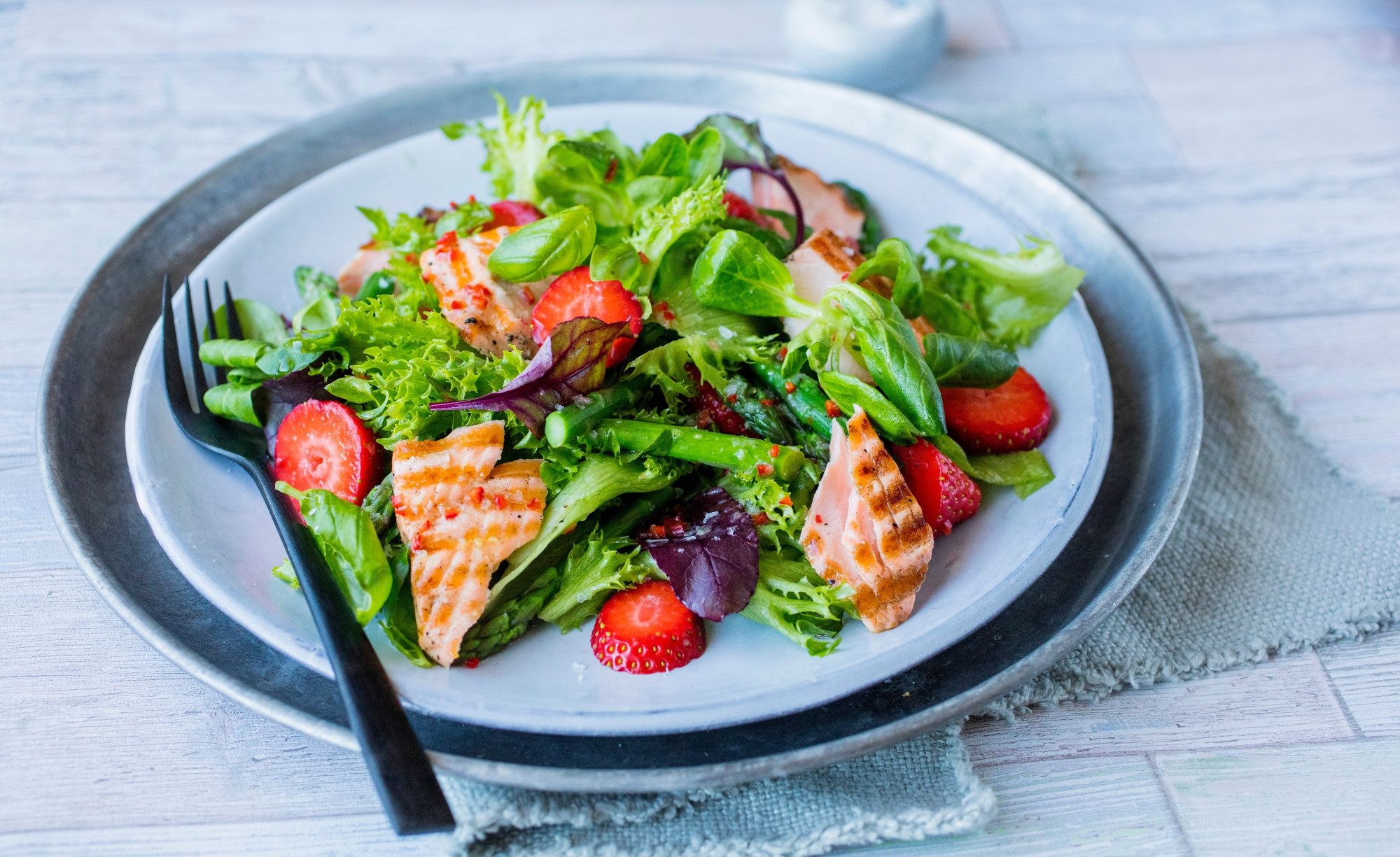 En frisk salat med grønne blader, asparges, skiveskåret laks og jordbær.