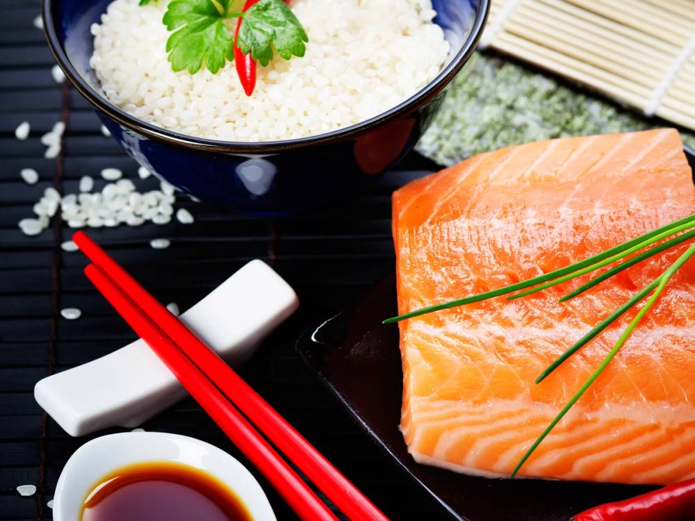 Sushibiter med rå laks, ris med koriander, soyasaus og spisepinner på en svart bakgrunn.