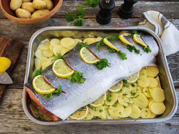 Hel laks med sitron- og urtekrydder på en seng av skivede poteter i en ildfast form.