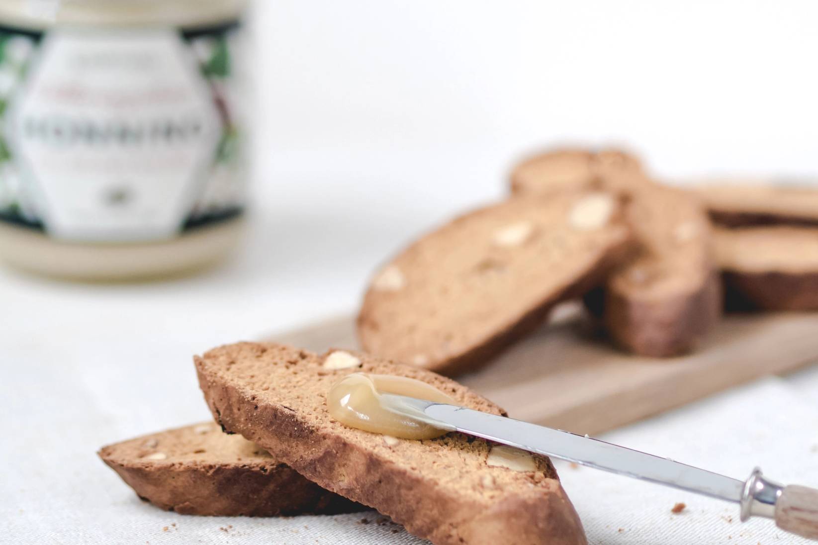 Skiver av brød med honning på en treplate, med en skje som har honning på seg.