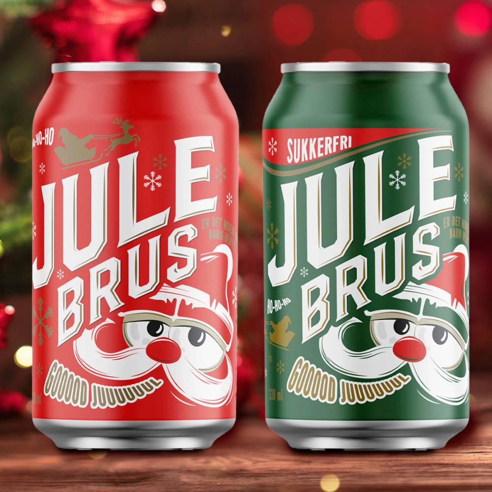 To bokser med julebrus, en rød og en grønn, plassert på et bord med julepynt i bakgrunnen.