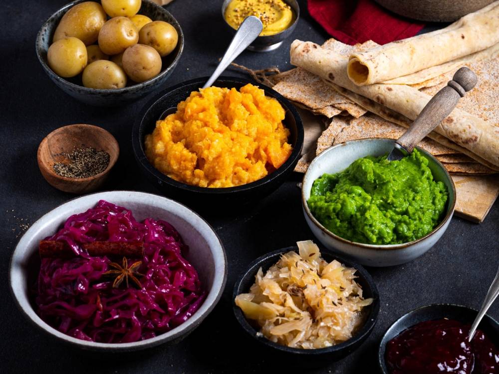 Ulike juletilbehør som poteter, rødkål, surkål, grønnsaker og julekaker på et bord.