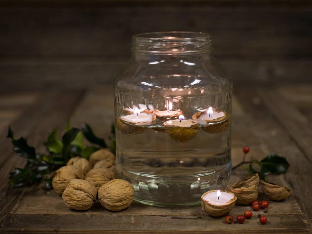 Et glass med vann og flytende lys, omgitt av nøtter og små røde bær, på en treoverflate.