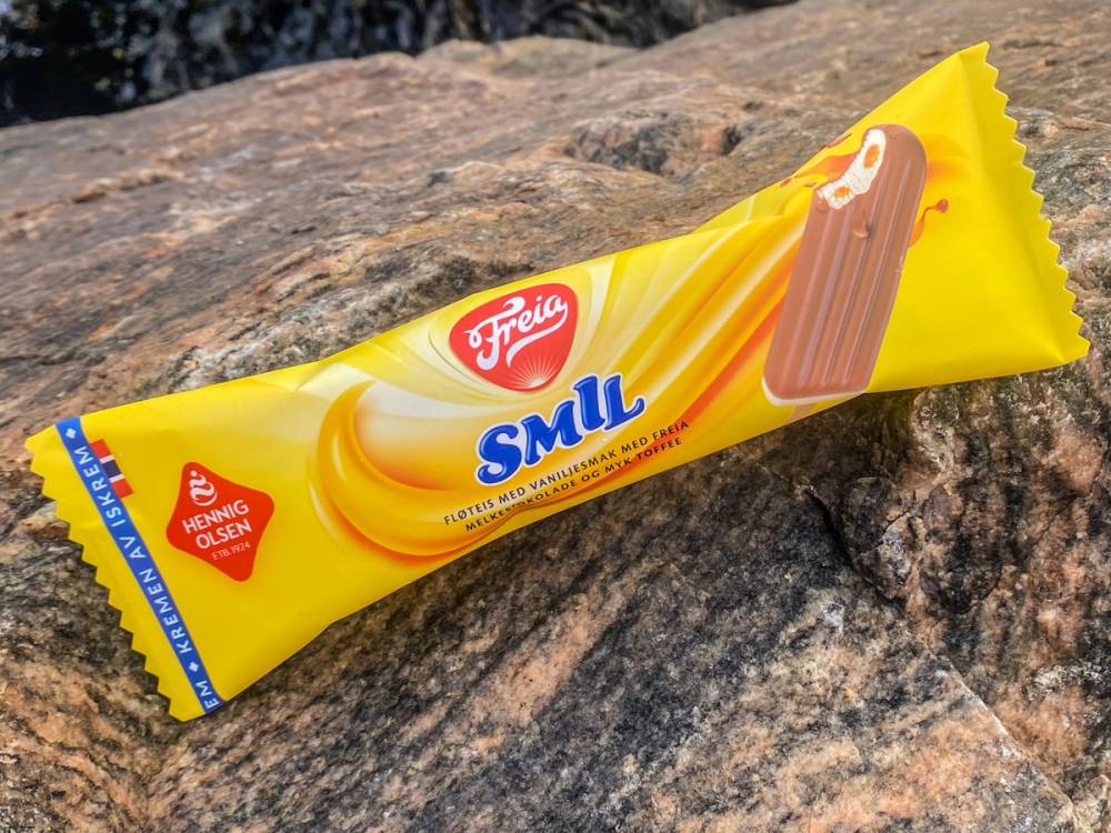 En gul pakke med Freia Smil sjokolade på en stein, med et bilde av en sjokoladebar på pakken.