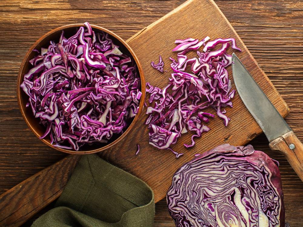 Skivet rødkål på skjærebrett med kniv, klar til å brukes i matlaging.