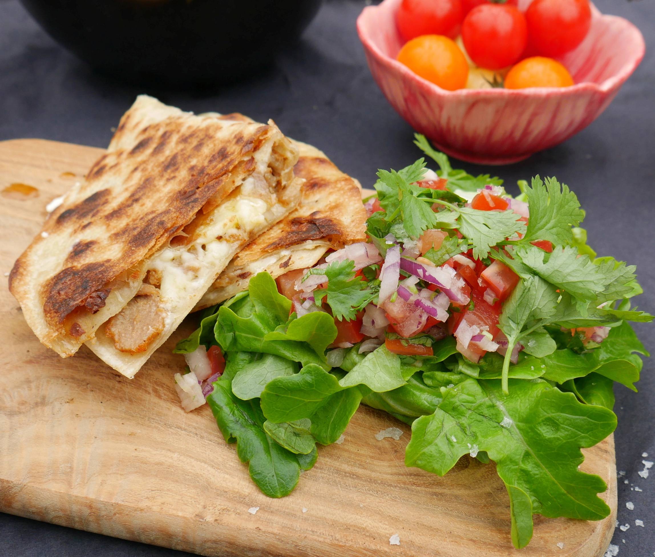 En tallerken med fylt naanbrød og en frisk salat med tomater og urter, plassert på et treplate.
