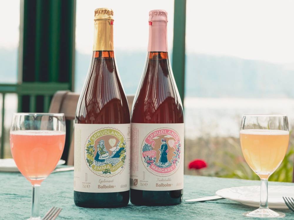 To flasker med rosévin på et bord med to glass fylt med rosévin, med en utsikt over vann og fjell i bakgrunnen.