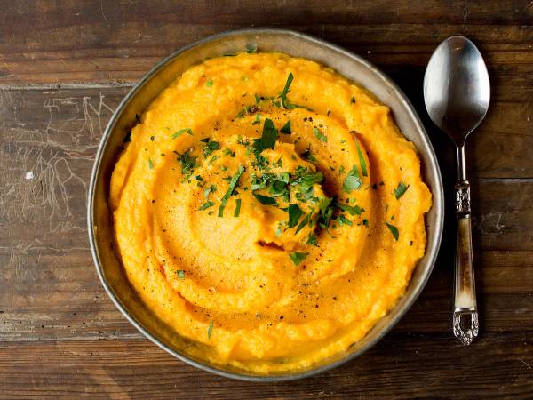 Kaalrotstappe ser ut som en gul, kremet rett pyntet med hakket grønt på en rustikk treflate, med en skje ved siden av.