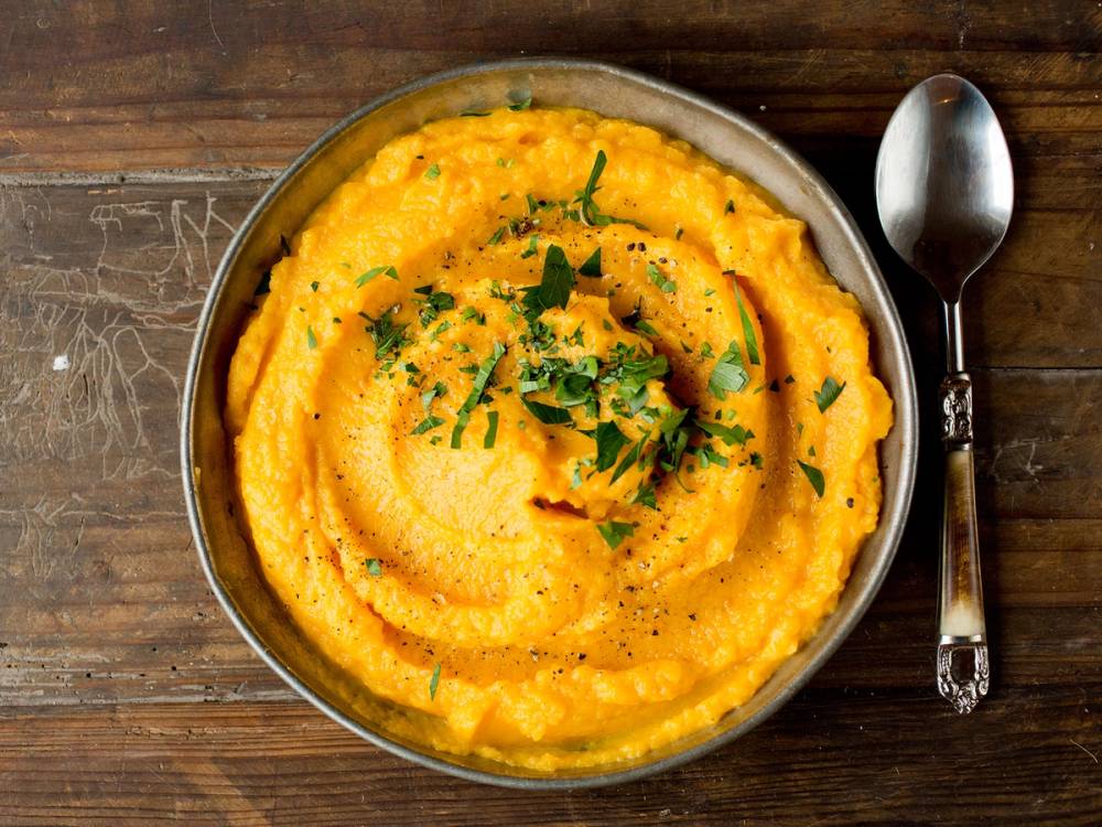 Kaalrotstappe ser ut som en gul, kremet rett pyntet med hakket grønt på en rustikk treflate, med en skje ved siden av.