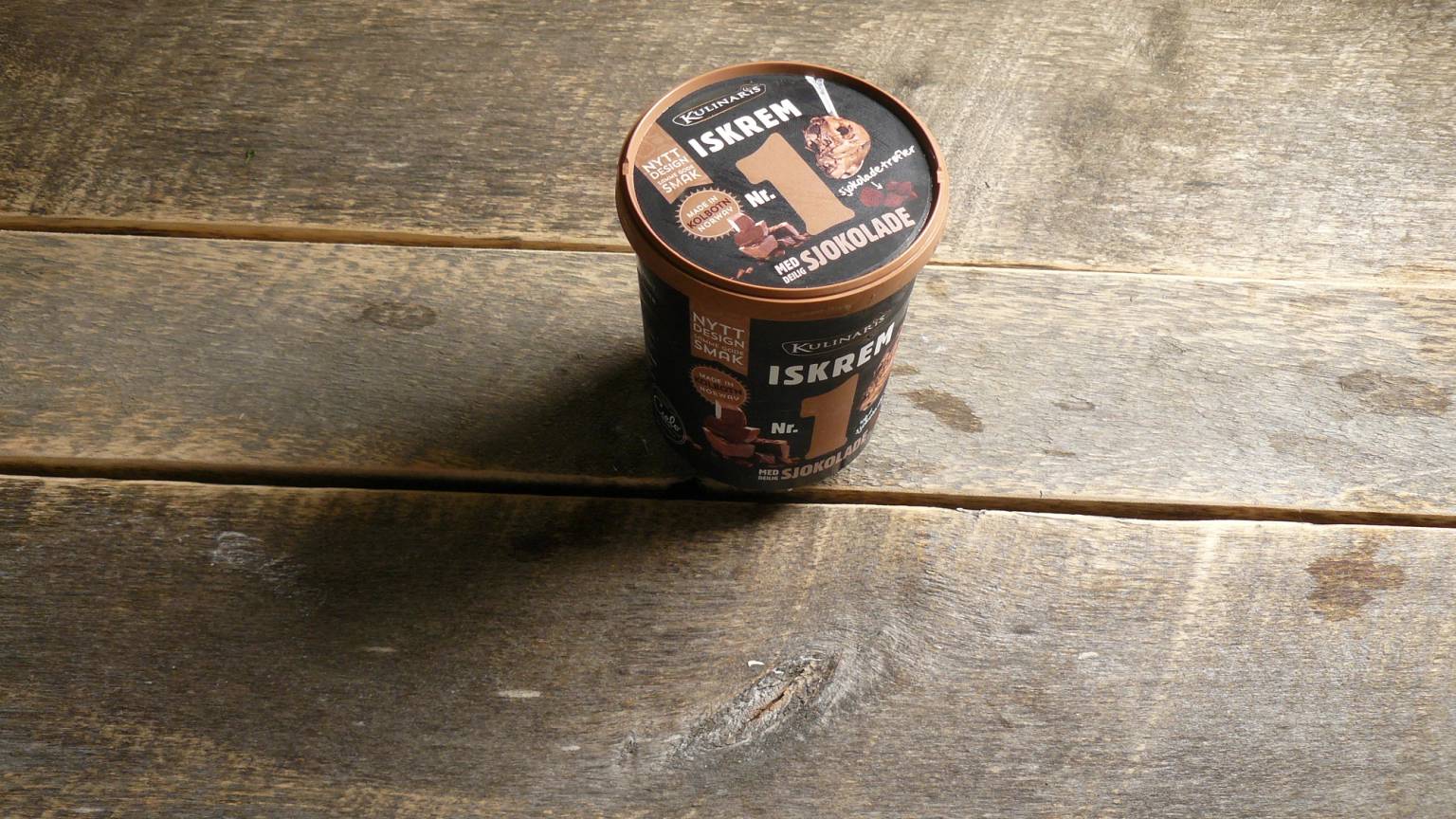 En kopp med iskrem plassert på et trebord, med en etikett som sier 'ISKRIG'.