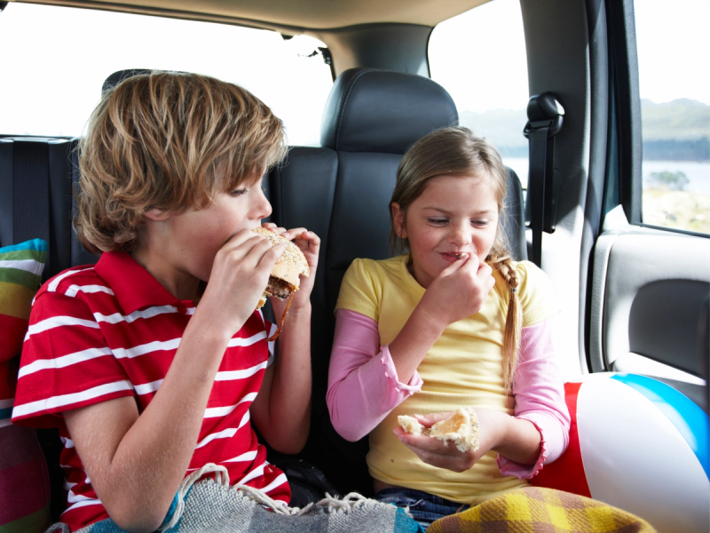 To barn som spiser snacks i baksetet av en bil under en bilferie.
