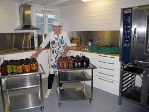 Person i kjøkken med flere glass med syltetøy eller gelé på en benk, og et stort ovn eller komfyr til høyre.