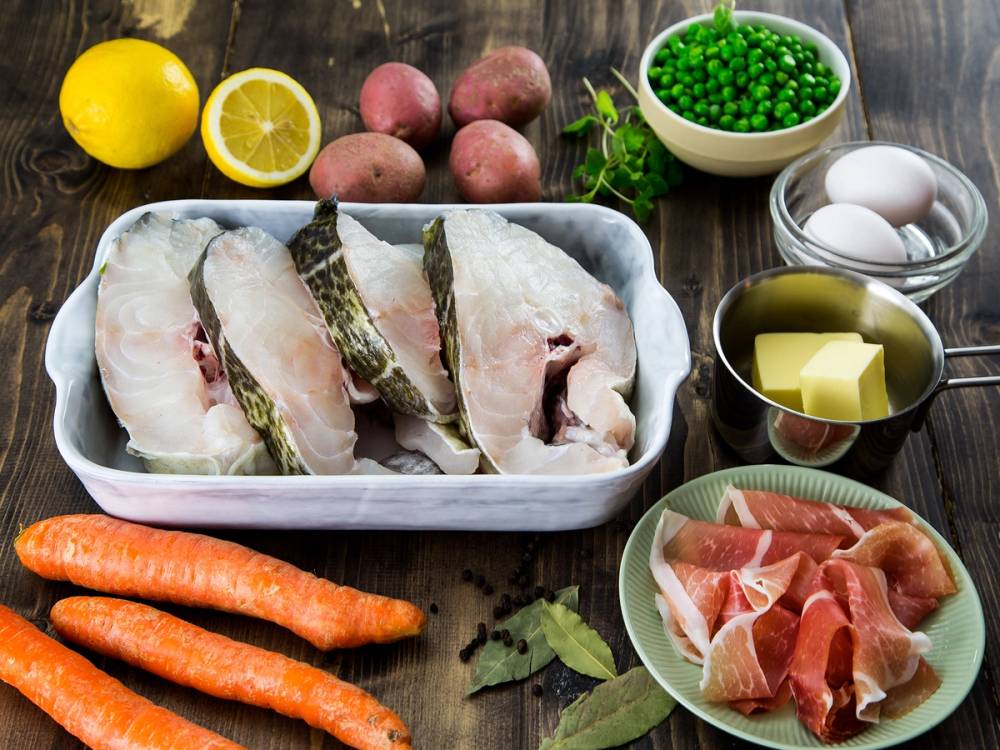 Ferske skreifileter med grønnsaker, poteter, egg og smør på et kjøkkenbord.