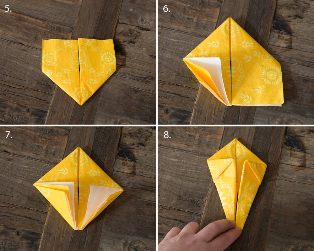 En gul påskeserviett er brettet til en påskehare i flere steg, med synlige brettelinjer og foldinger.