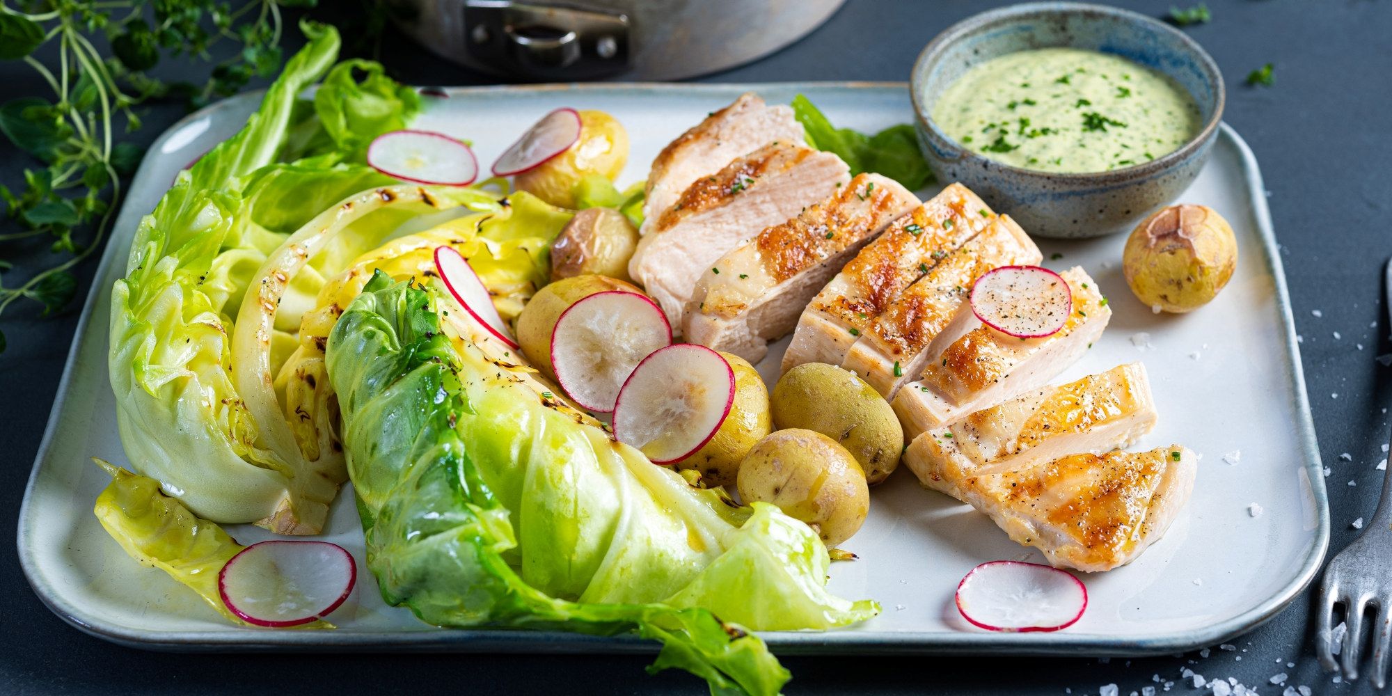 Kyllingbryst med salat og bakte nypoteter på en tallerken, med en liten skål med saus ved siden av.