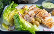 Kyllingbryst med salat og bakte nypoteter på en tallerken, med en liten skål med saus ved siden av.