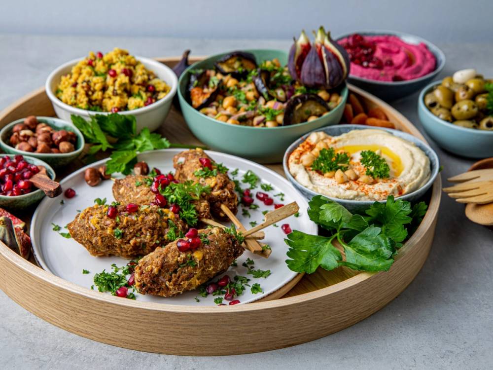 Et utvalg av ulike retter og tilbehør på en rund treplate, inkludert falafel, hummus, salat og oliven.