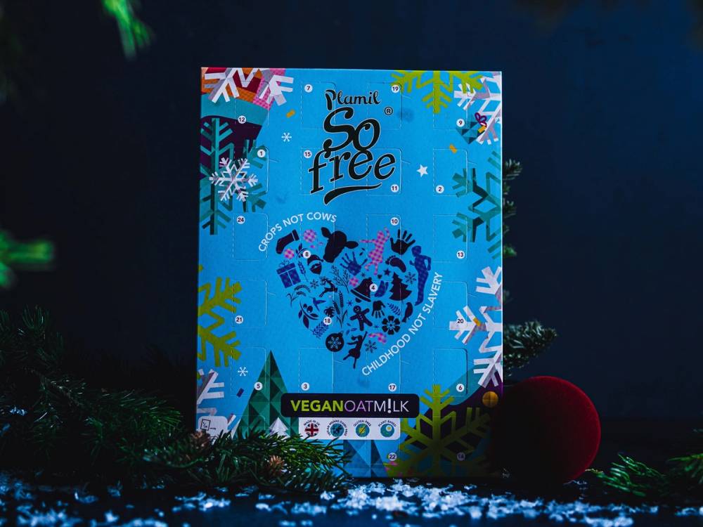 En blå kalender med teksten 'So free' og ulike vinter- og juledekorasjoner, plassert på en mørk bakgrunn med noe grønt og en rød ball i nærheten.