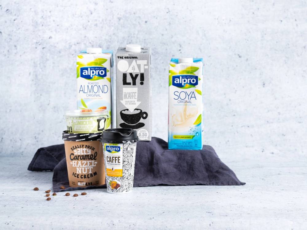 Et utvalg av plantemelk og kaffeprodukter fra Alpro og Oatly, plassert på en mørk duk mot en lys bakgrunn.