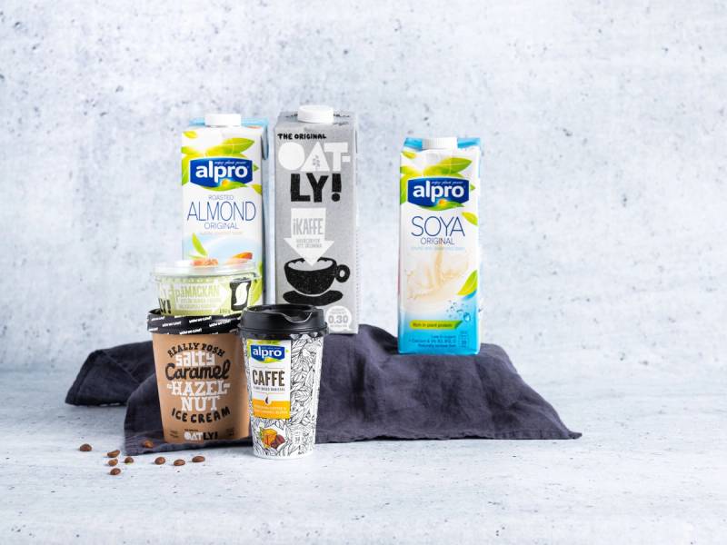 Et utvalg av plantemelk og kaffeprodukter fra Alpro og Oatly, plassert på en mørk duk mot en lys bakgrunn.